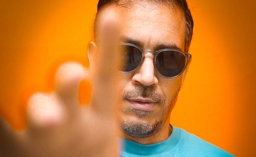 Atef Khelili with sunglasses and a blue shirt is making a peace sign.